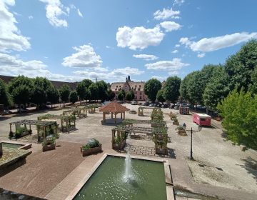 Photo qui montre la place du château avec tous les bacs à plantes installés, le kiosque en plein centre de la place et un point d’eau en premier plan.